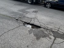 A close up of a street with a cracked pothole in the middle, which is full of rain water.